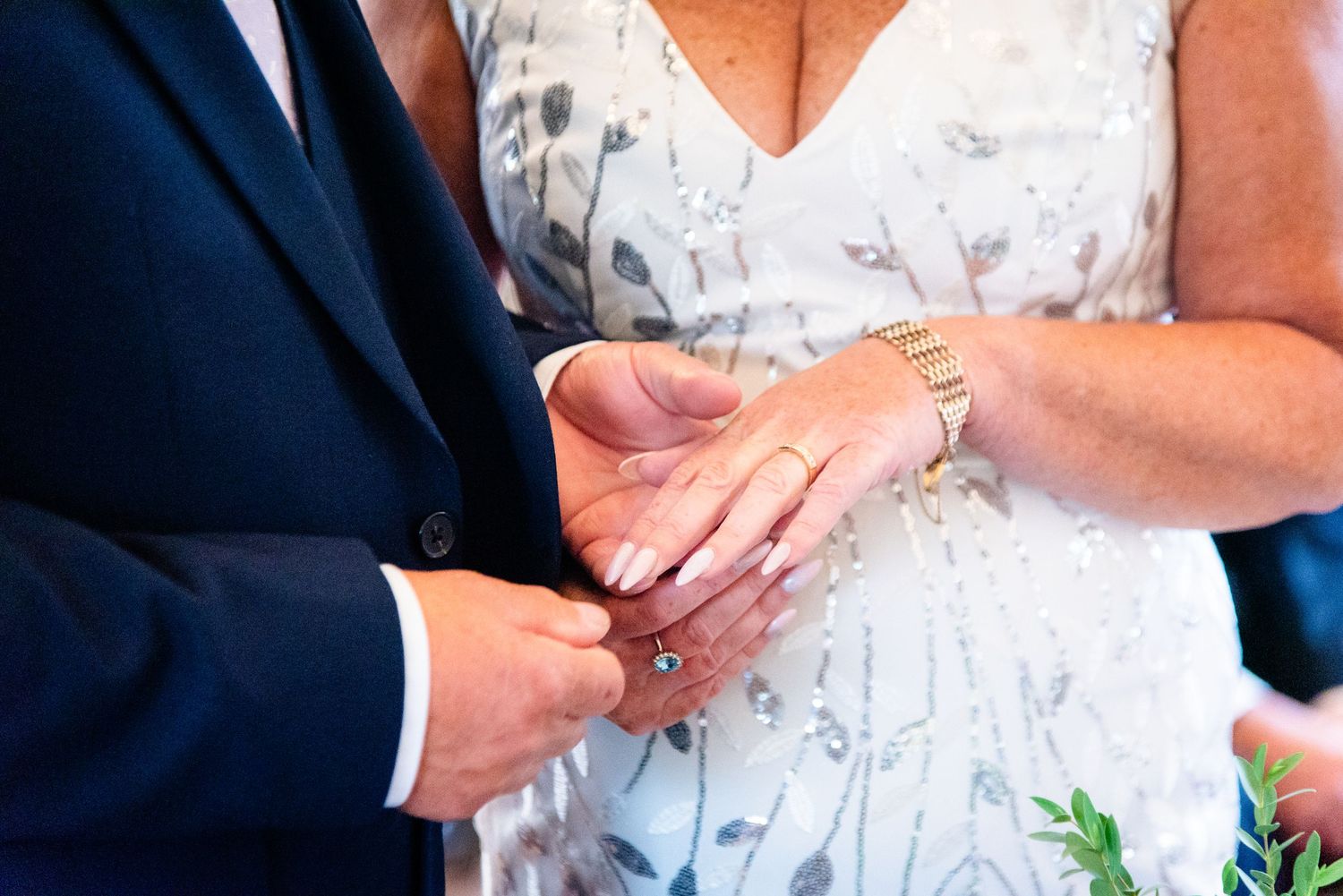 Couple exchanging wedding rings during marriage ceremony, close-up of hands with gold watch and elegant white dress.