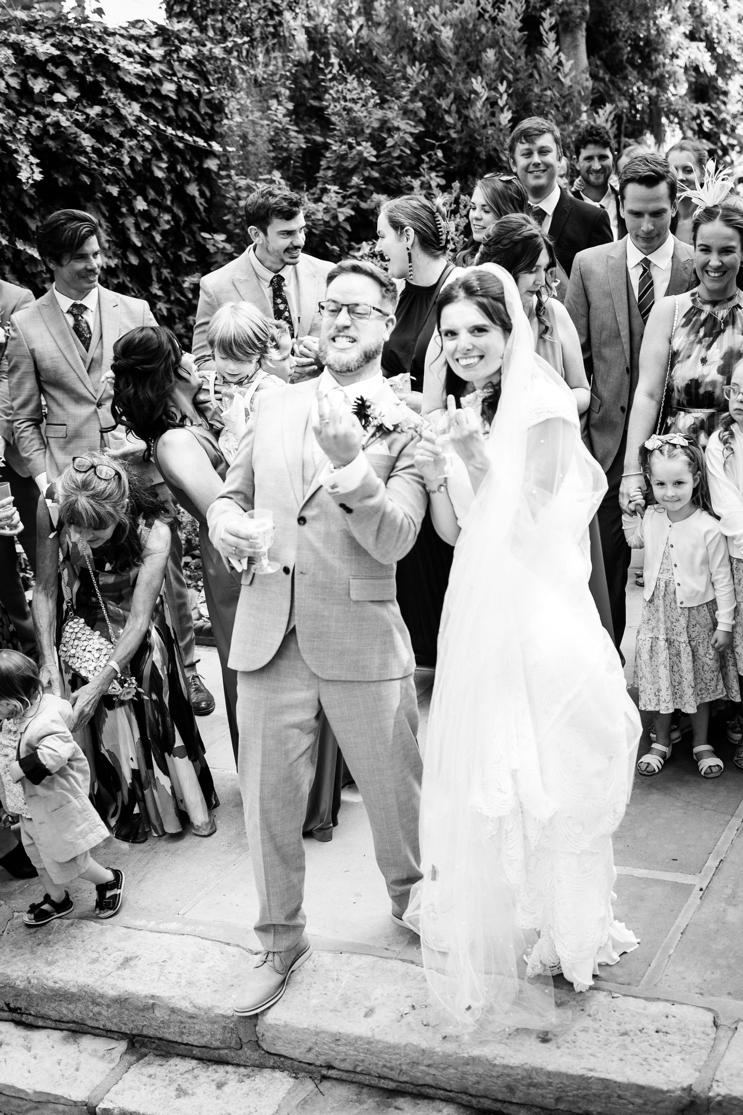 Black and white photo of a joyful bride and groom celebrating with guests outside.