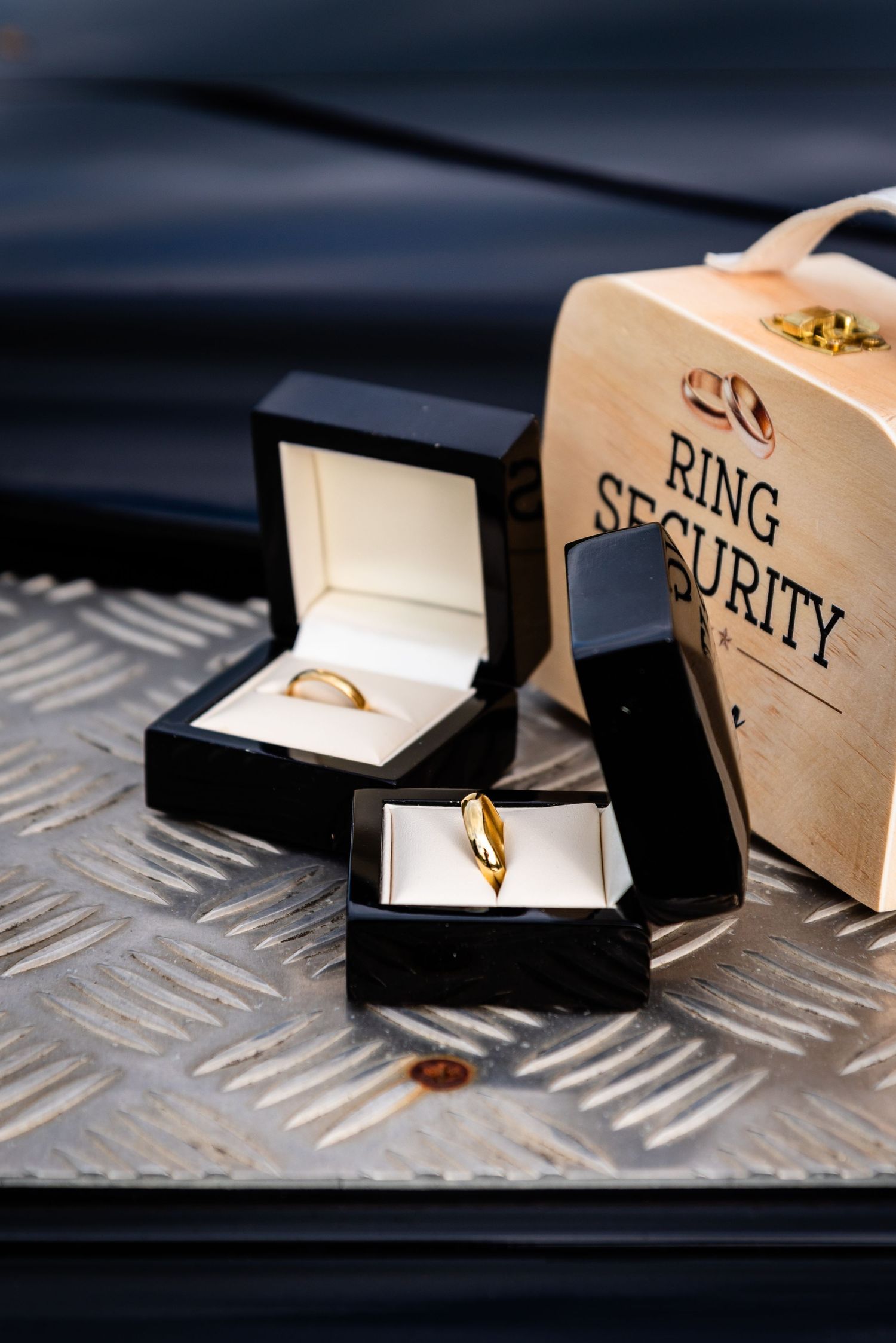 Two gold wedding rings displayed in black velvet boxes beside a wooden Ring Security briefcase.
