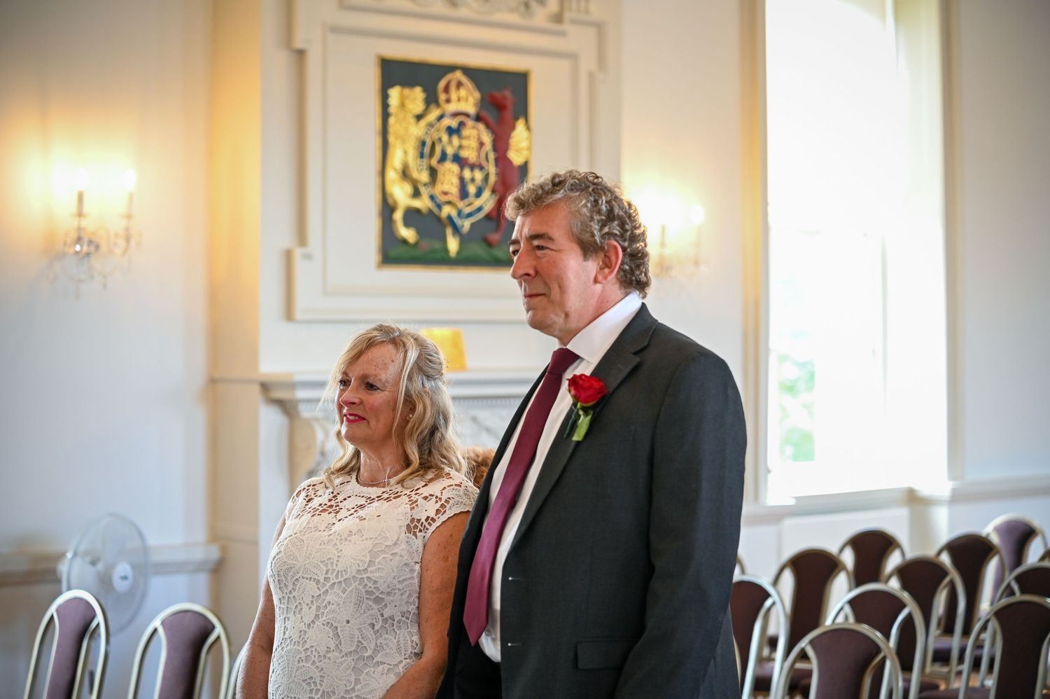 Bride and groom standing together during wedding ceremony in elegant white room with royal coat of arms.