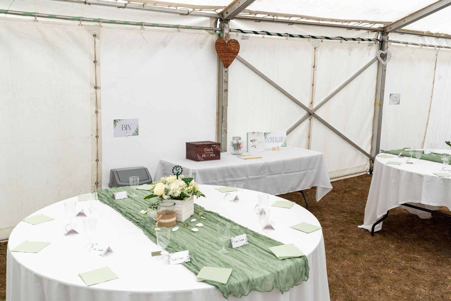 Elegant wedding reception tent with round tables dressed in white linens and sage green runners with floral centerpieces.