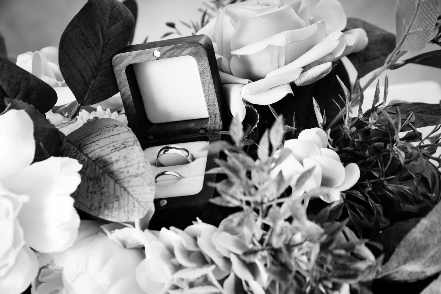Black and white close-up of wedding rings in a box nestled among beautiful flowers.