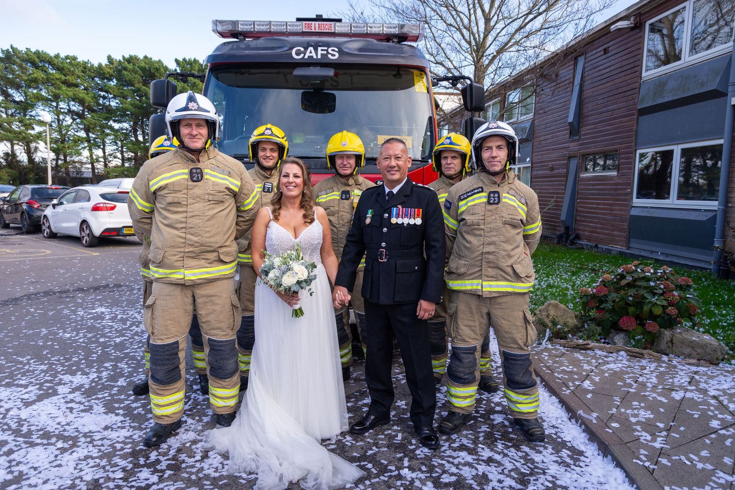 Bride and groom in military uniform pose with firefighters in front of a CAFS fire truck.