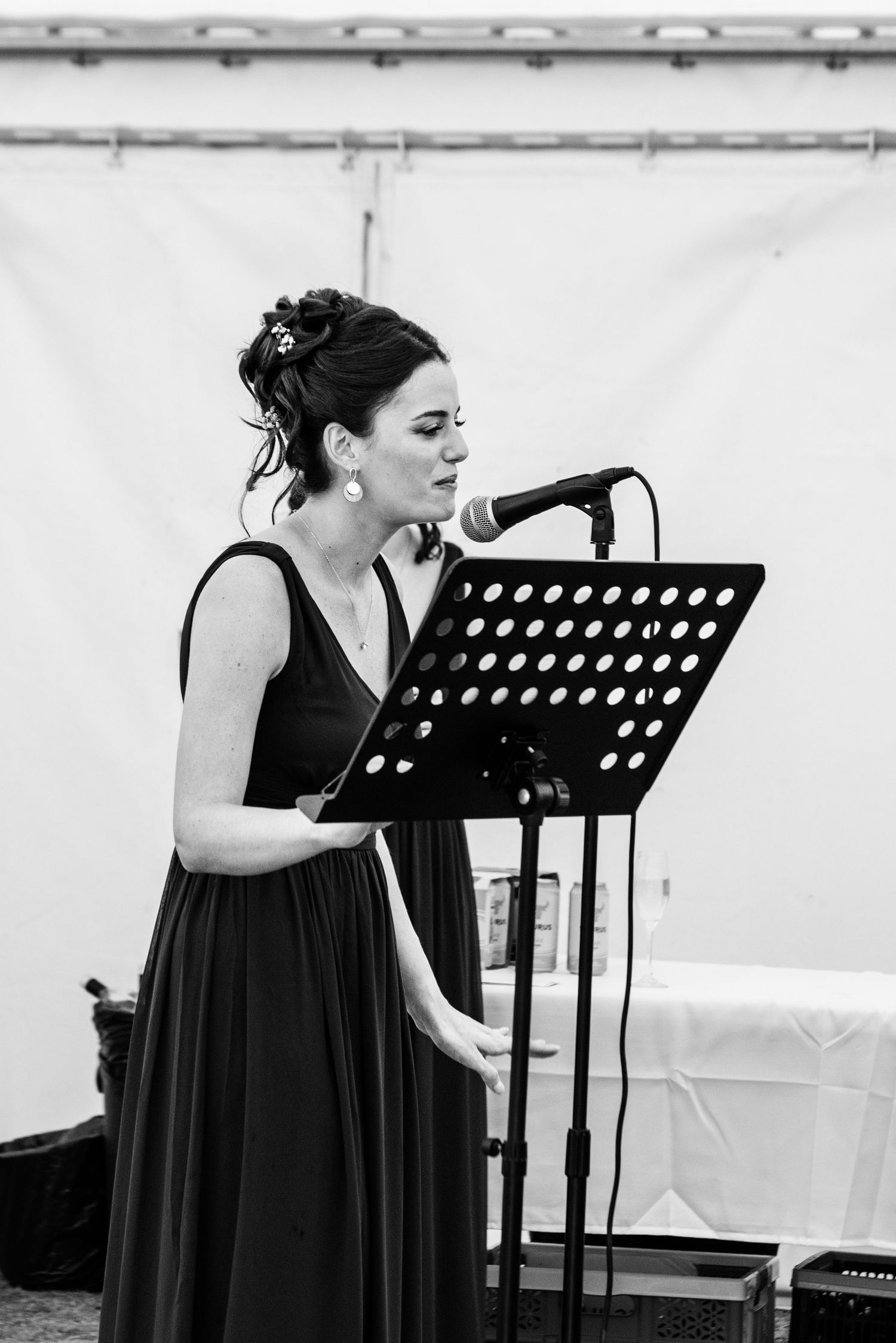 Woman in black dress singing at microphone stand with sheet music outdoors at event.