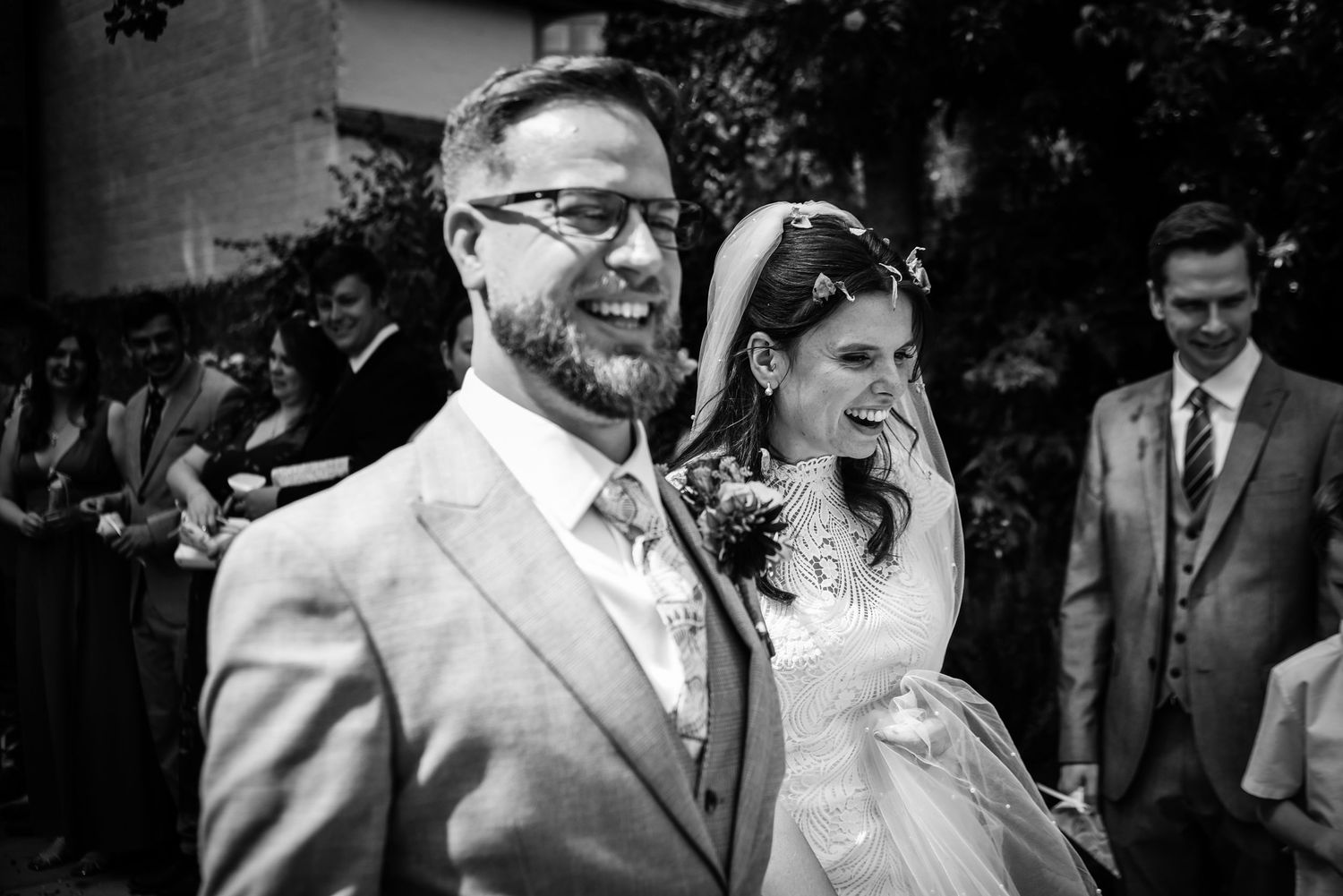 Black and white wedding photo showing happy couple at their ceremony with a groomsman in the background.