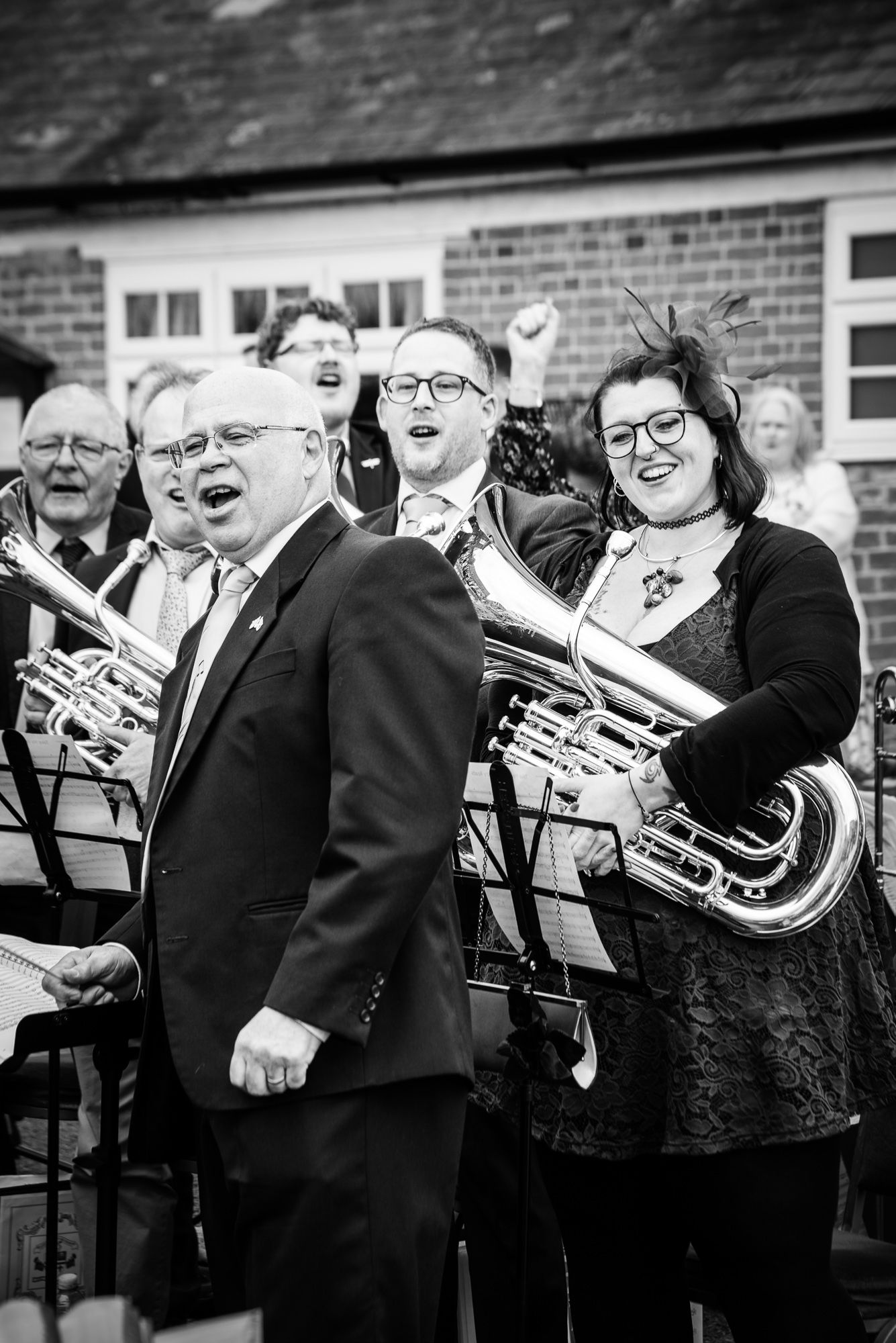 Black and white photo of brass band musicians performing outdoors, woman holding tuba in foreground.