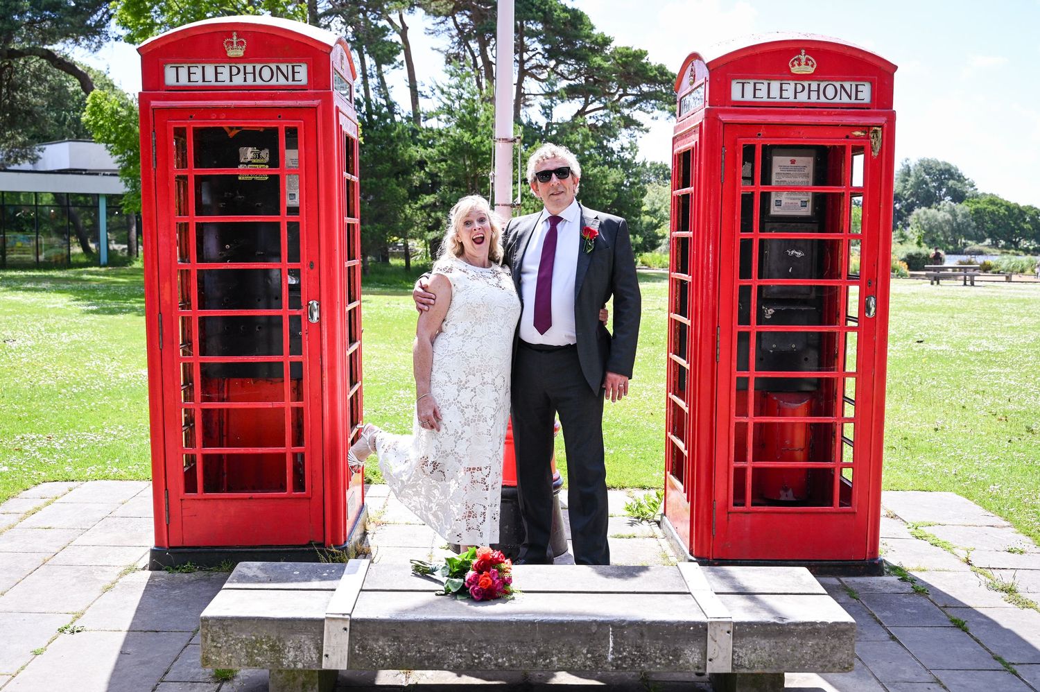 Couple posing between two classic red British telephone boxes outdoors on their wedding day.
