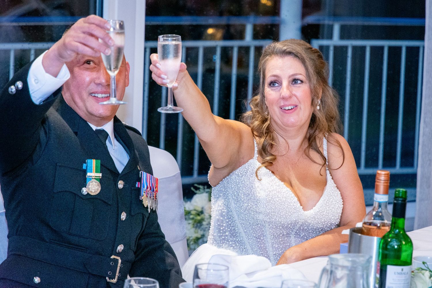 Bride and groom in military uniform raising champagne glasses in a wedding toast at their reception.
