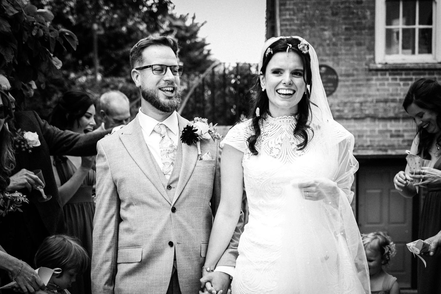 A black and white wedding photograph showing newlyweds holding hands and smiling after their ceremony.