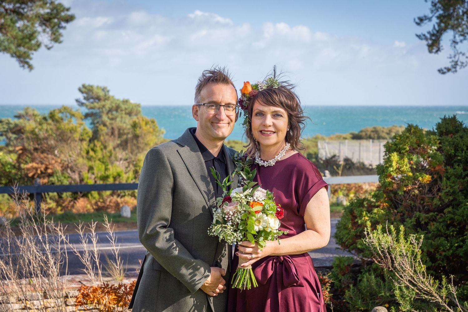 A couple poses together in a scenic outdoor setting with water and trees in the background.