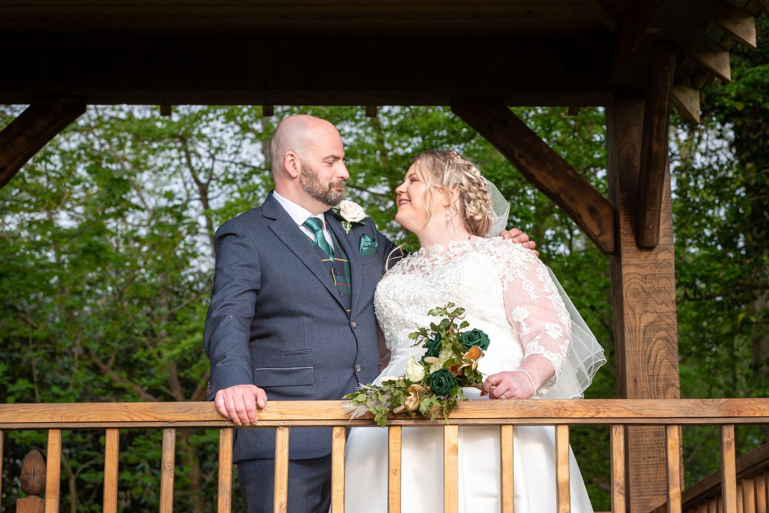 A couple shares a joyful moment together on a wooden gazebo deck surrounded by green trees.