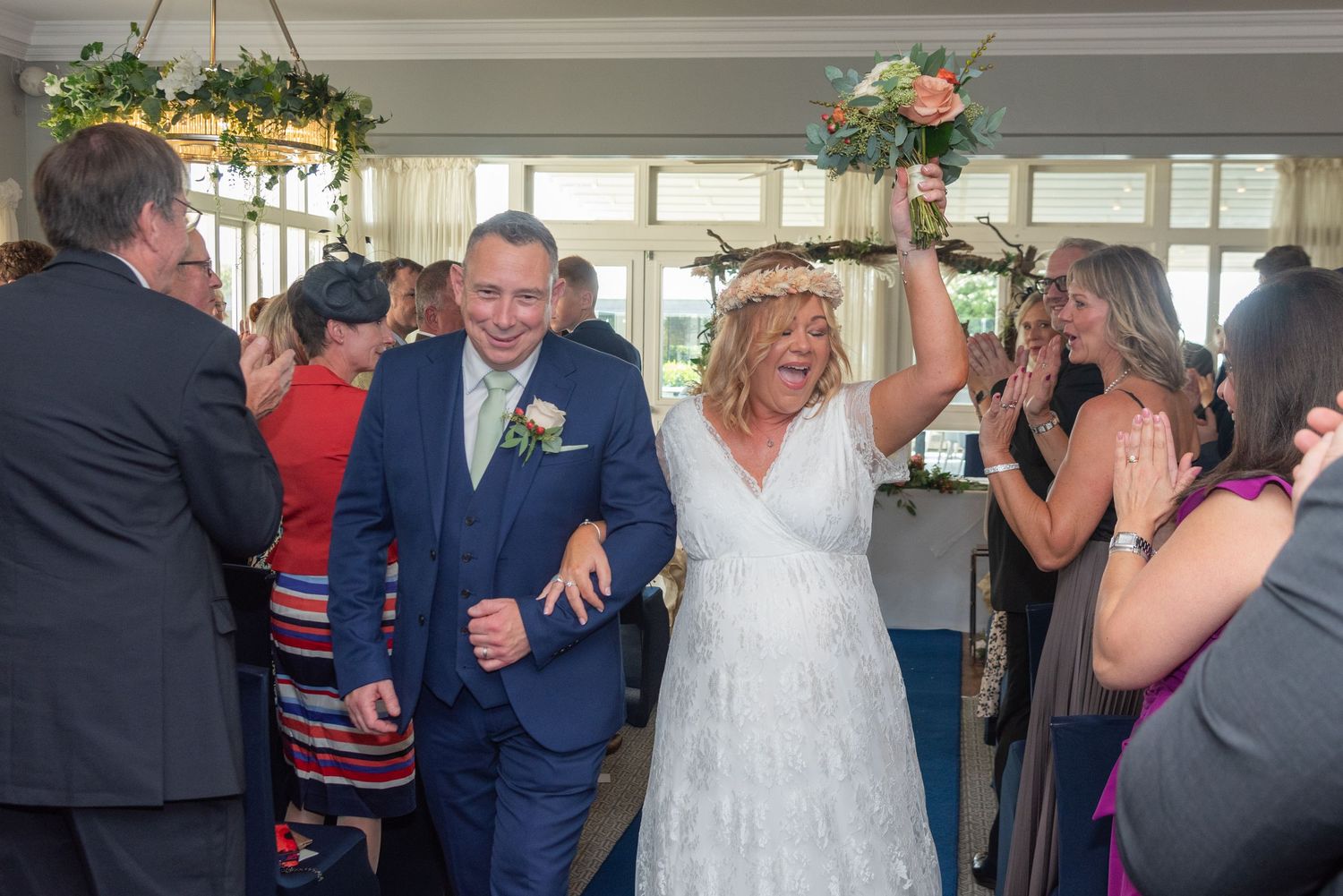 Joyful newlyweds walk down the aisle celebrating their wedding ceremony surrounded by cheering guests indoors.