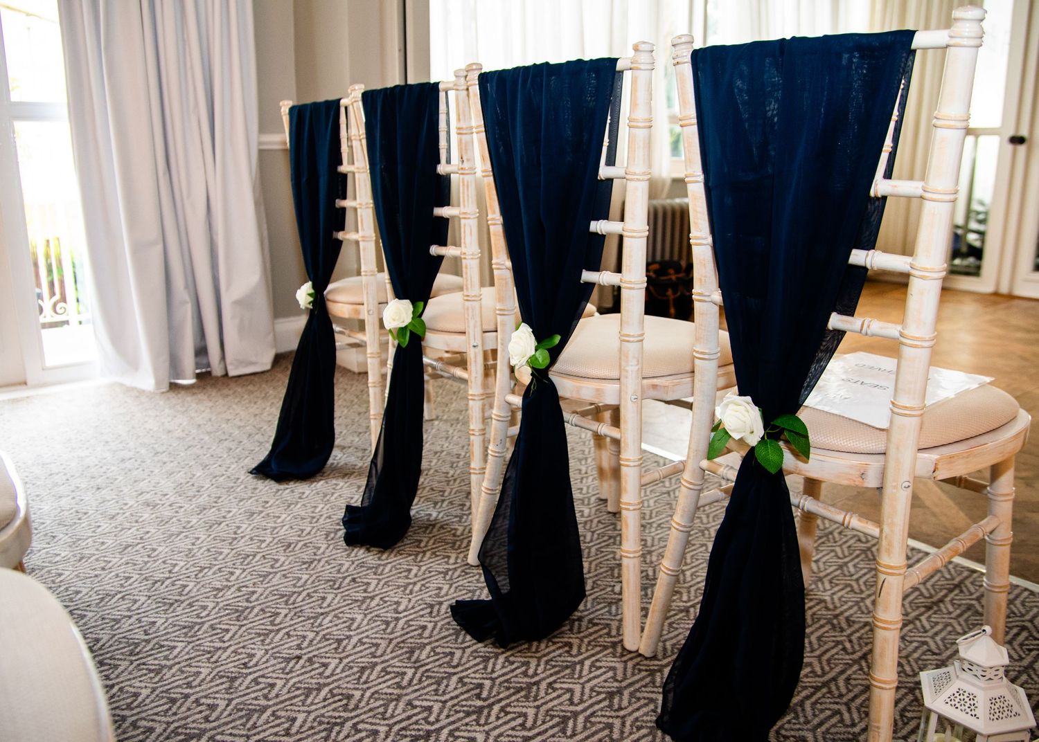 Elegant white Chiavari chairs decorated with navy blue sashes and white roses arranged in rows for a wedding ceremony.