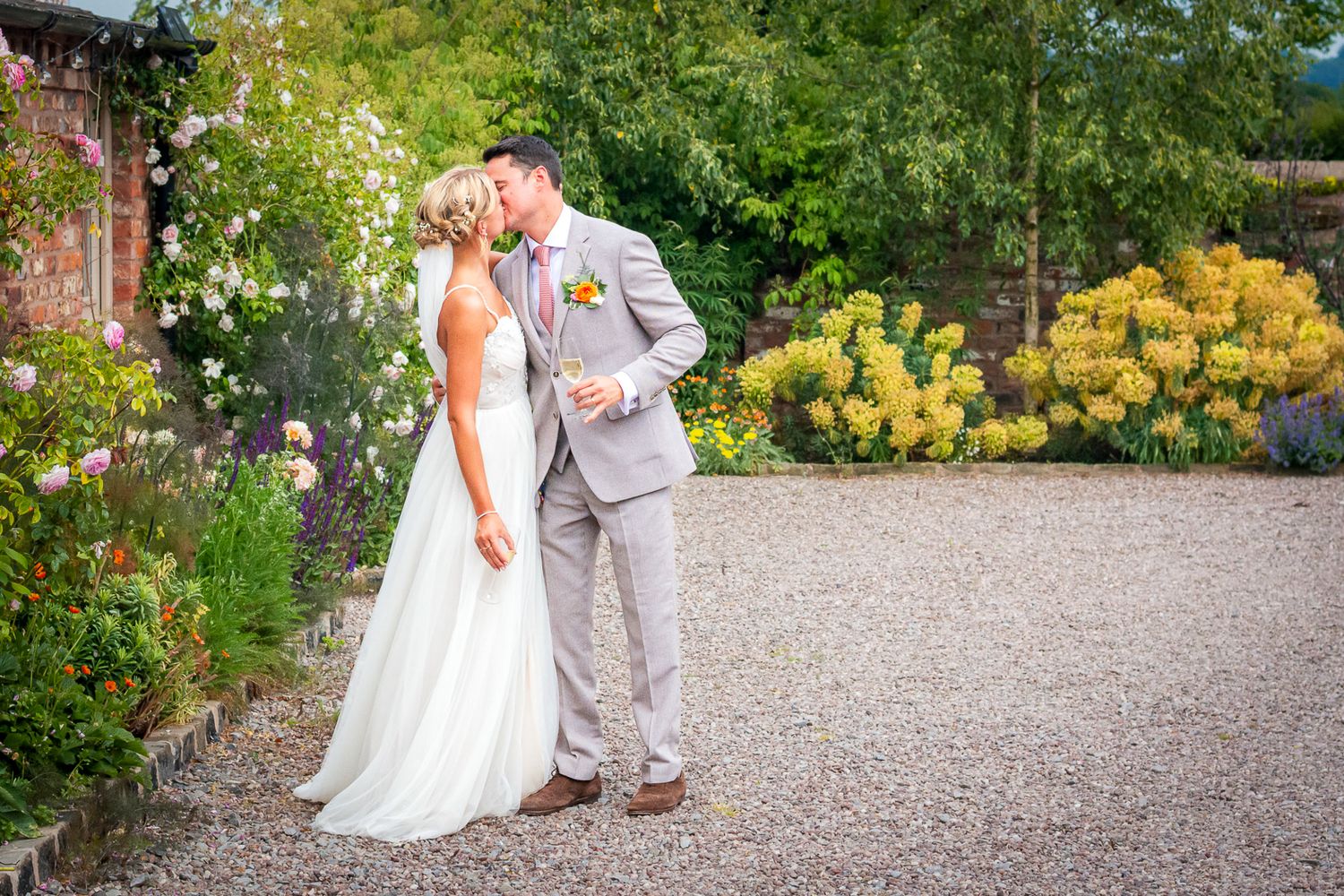 Bride and groom sharing a romantic moment in a lush garden, bride in white gown, groom in grey suit.