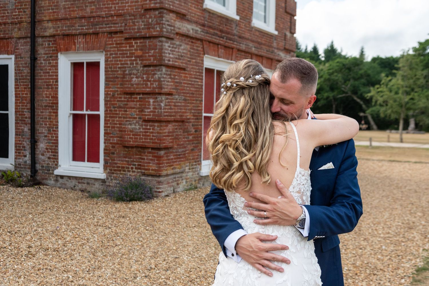 Bride and groom share tender embrace outside historic red brick wedding venue.