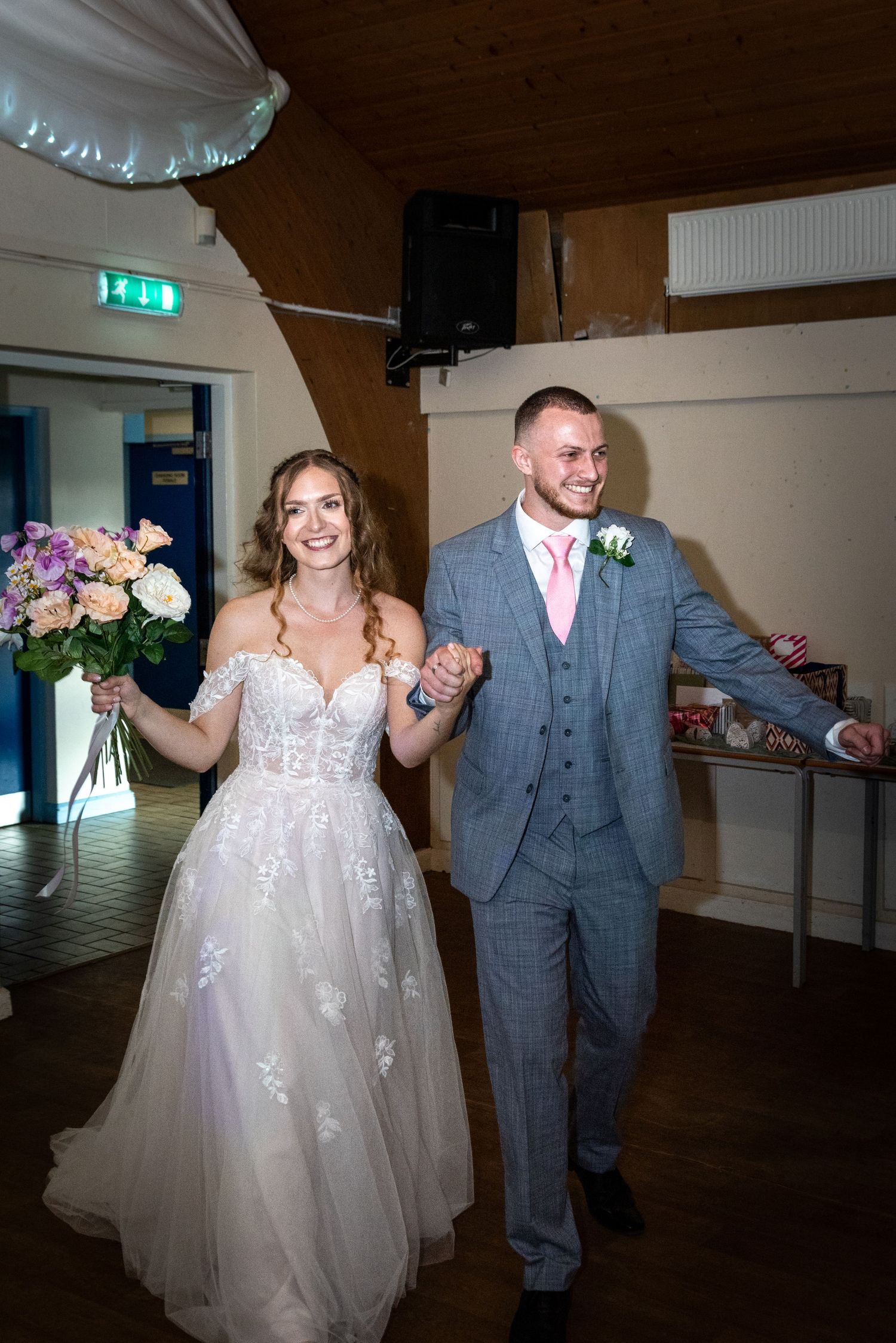 Happy bride and groom entering wedding reception holding hands and bouquet.