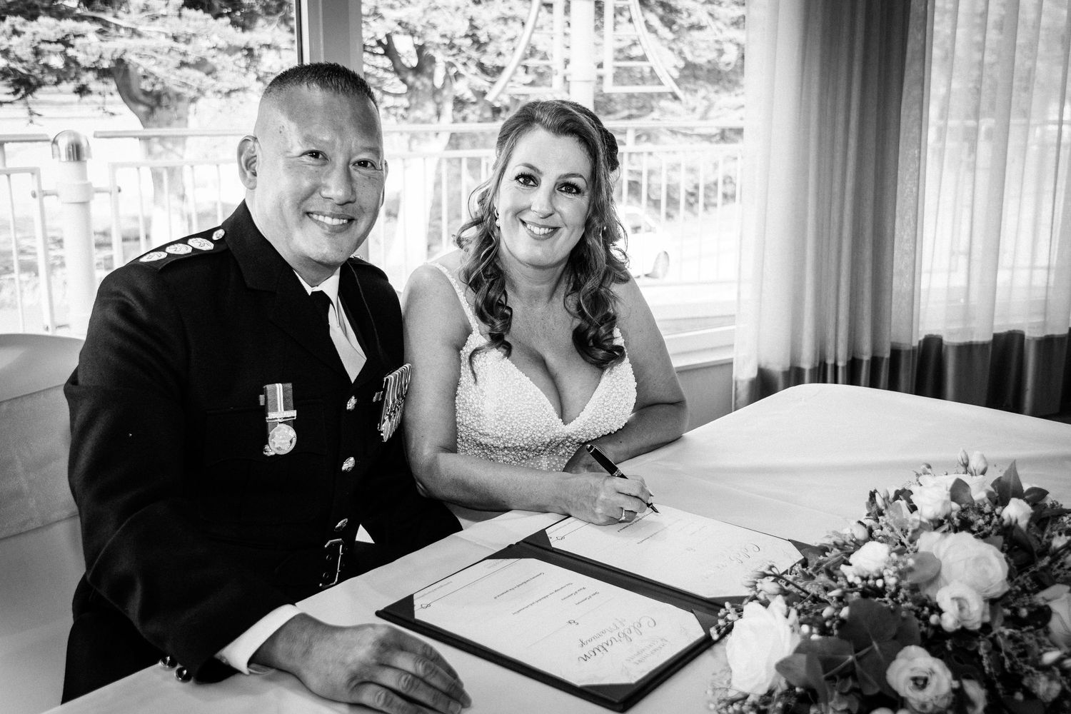 Bride and groom sign wedding register at table with flowers in elegant black and white portrait.