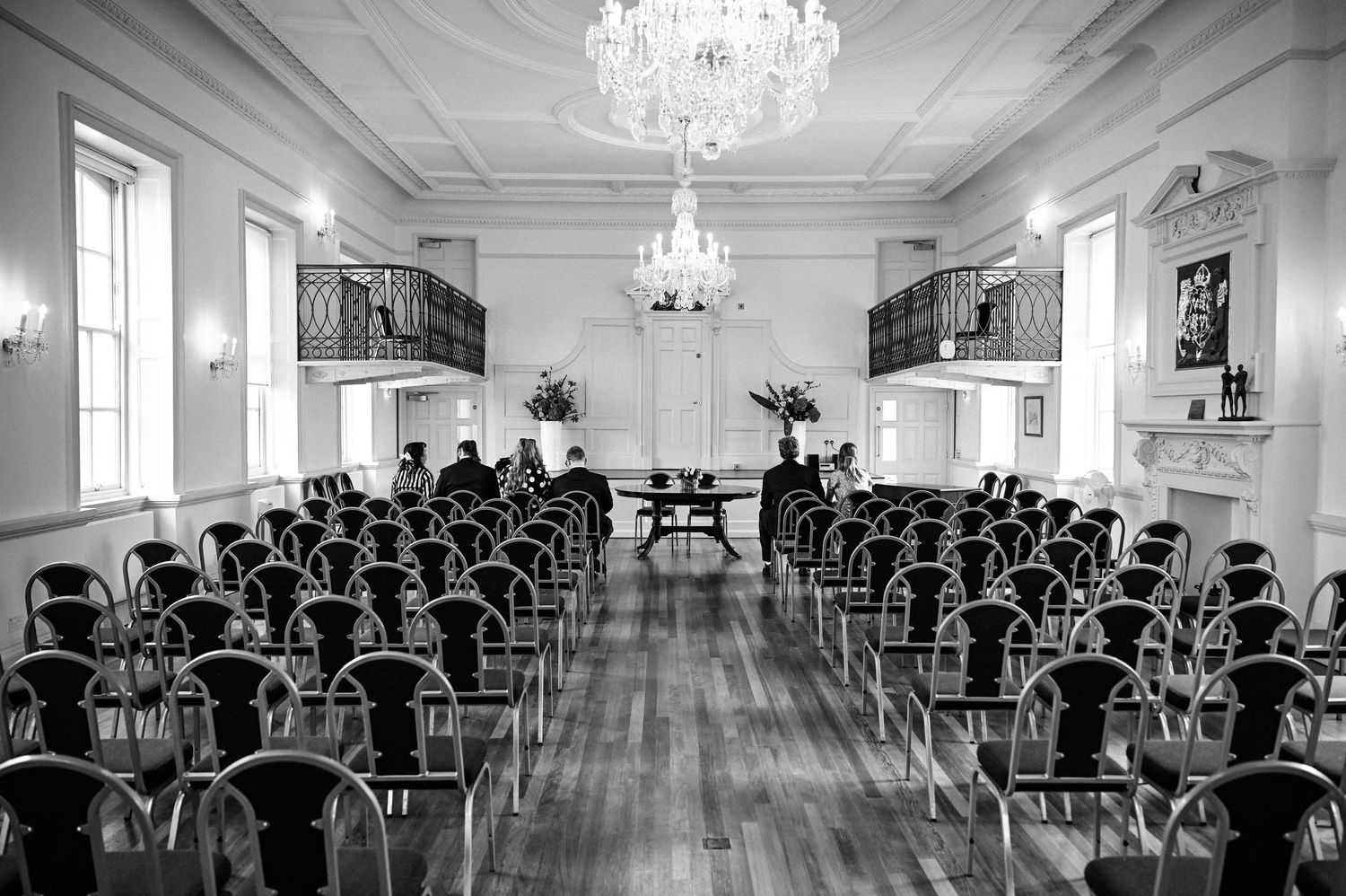 Elegant black and white photo of a grand ballroom set up for a wedding ceremony with rows of chairs and crystal chandeliers.