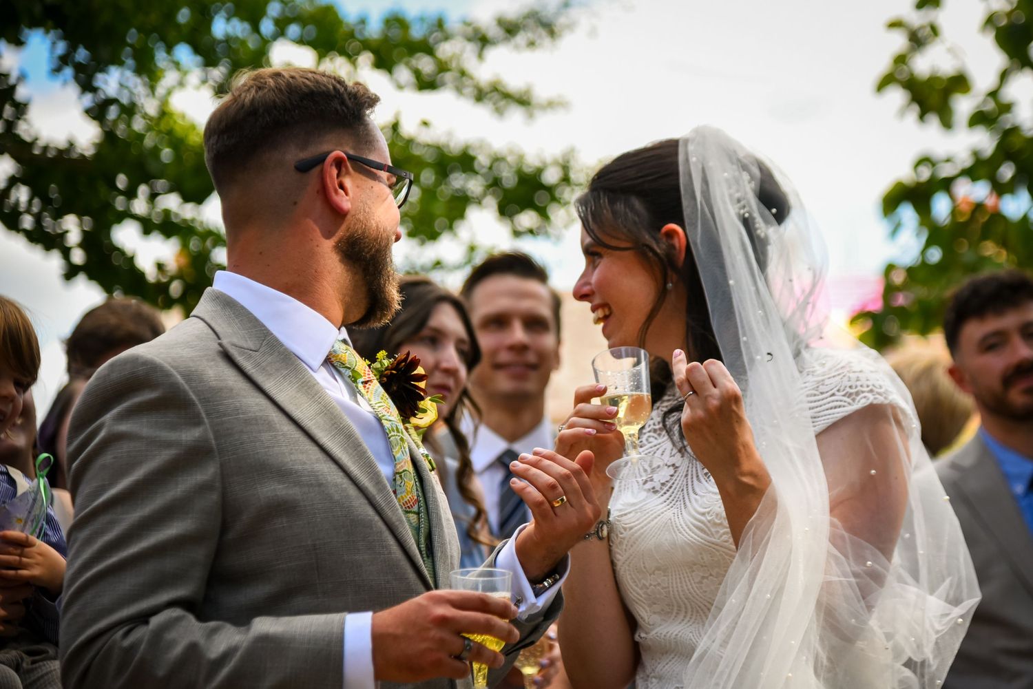 Bride and groom sharing a romantic moment with champagne at outdoor wedding reception.