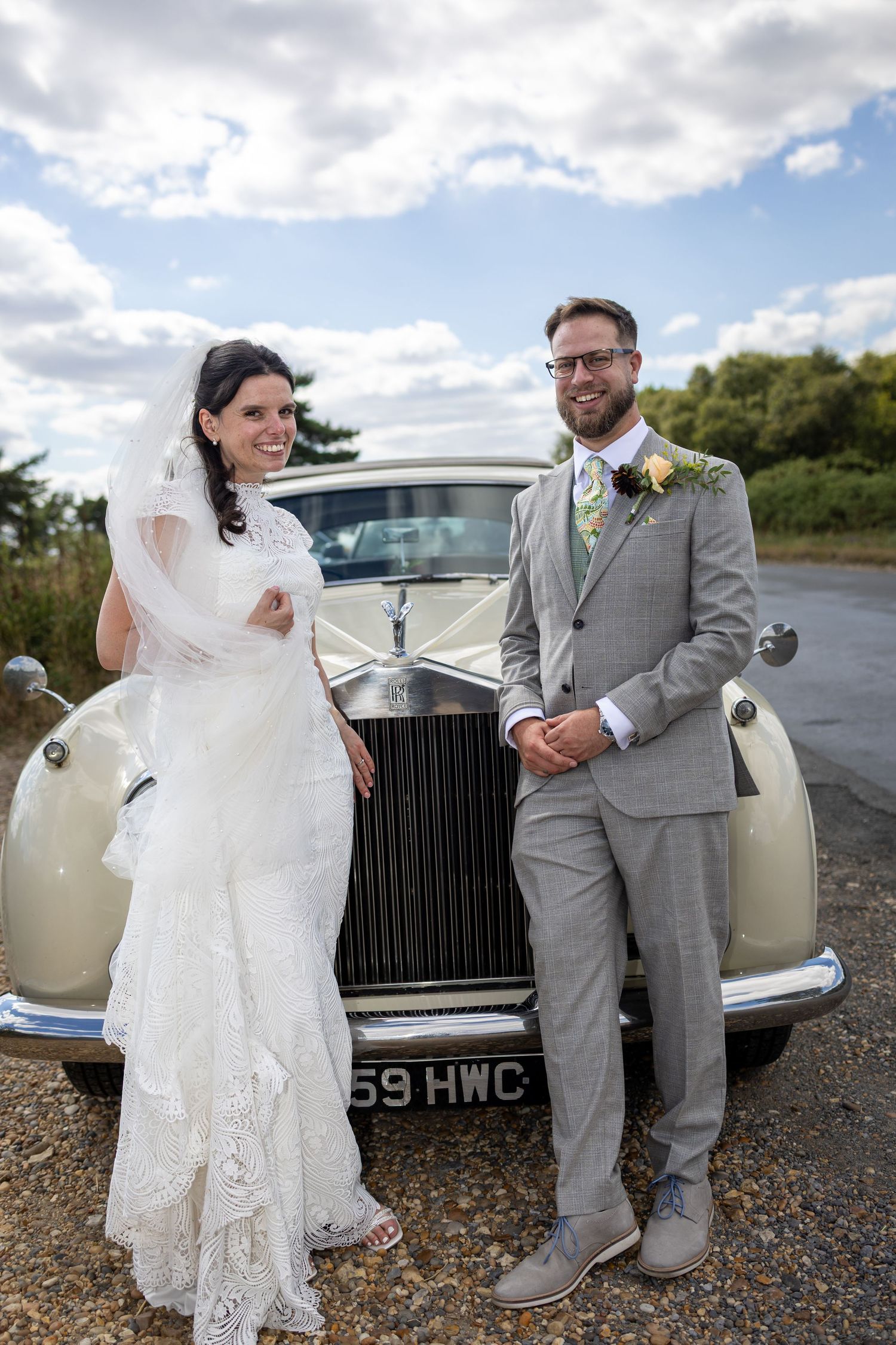Bride and groom stand together in front of a classic cream Rolls Royce.
