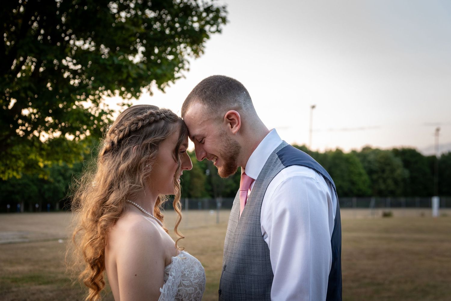 Bride and groom share romantic forehead touch at golden hour sunset in outdoor wedding portrait.