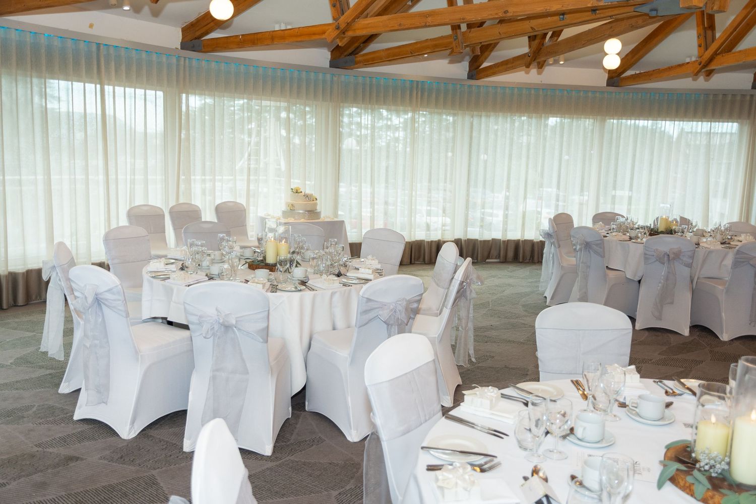 Elegant wedding reception venue with round tables, white chair covers, and soft natural lighting.