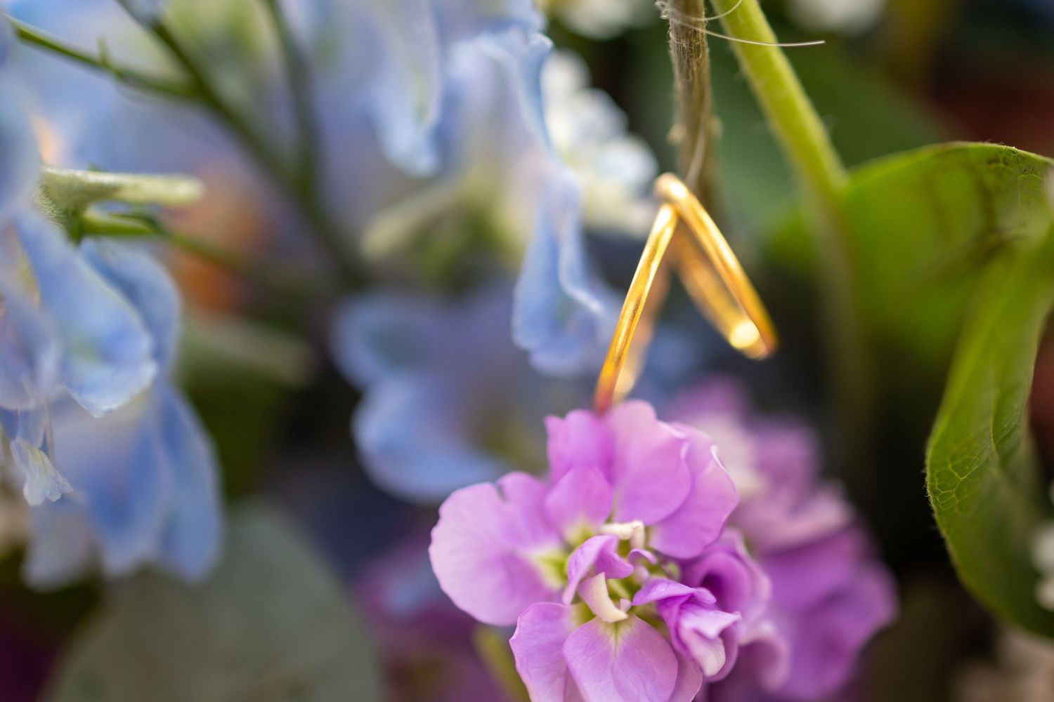 Gold rings hanging over blue and pink flowers in a soft-focus floral arrangement.