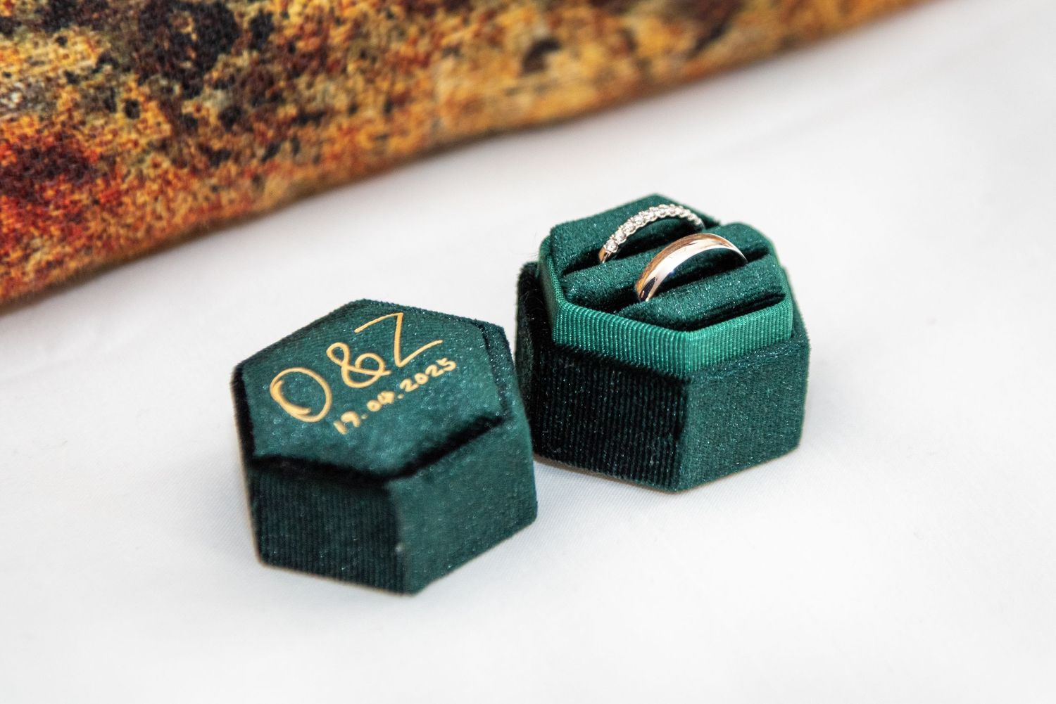 Green velvet hexagon ring box with gold monogram Q&Z holding two wedding bands.