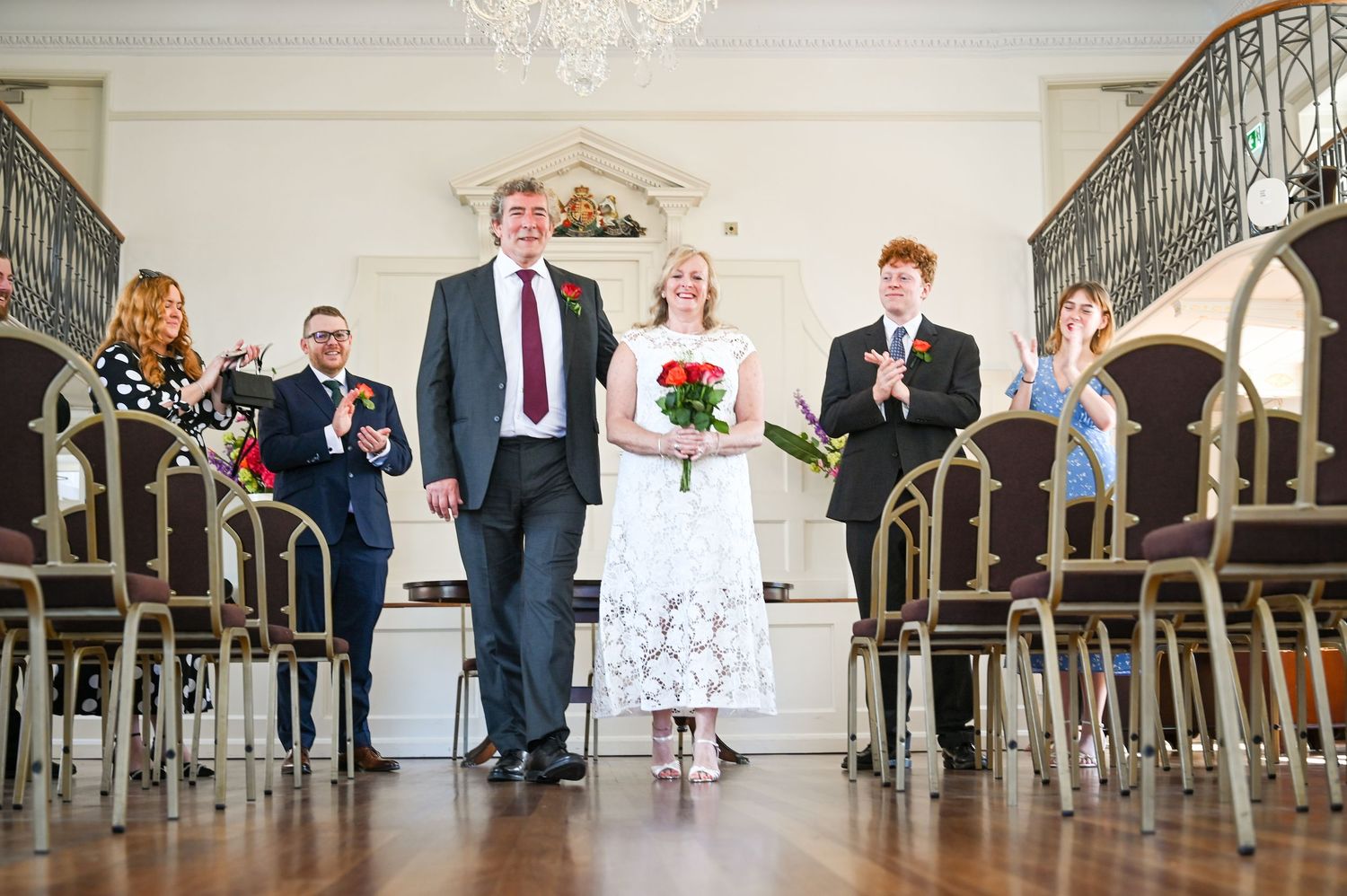 Newlywed couple walks down the aisle at elegant wedding ceremony while guests applaud in a grand hall.