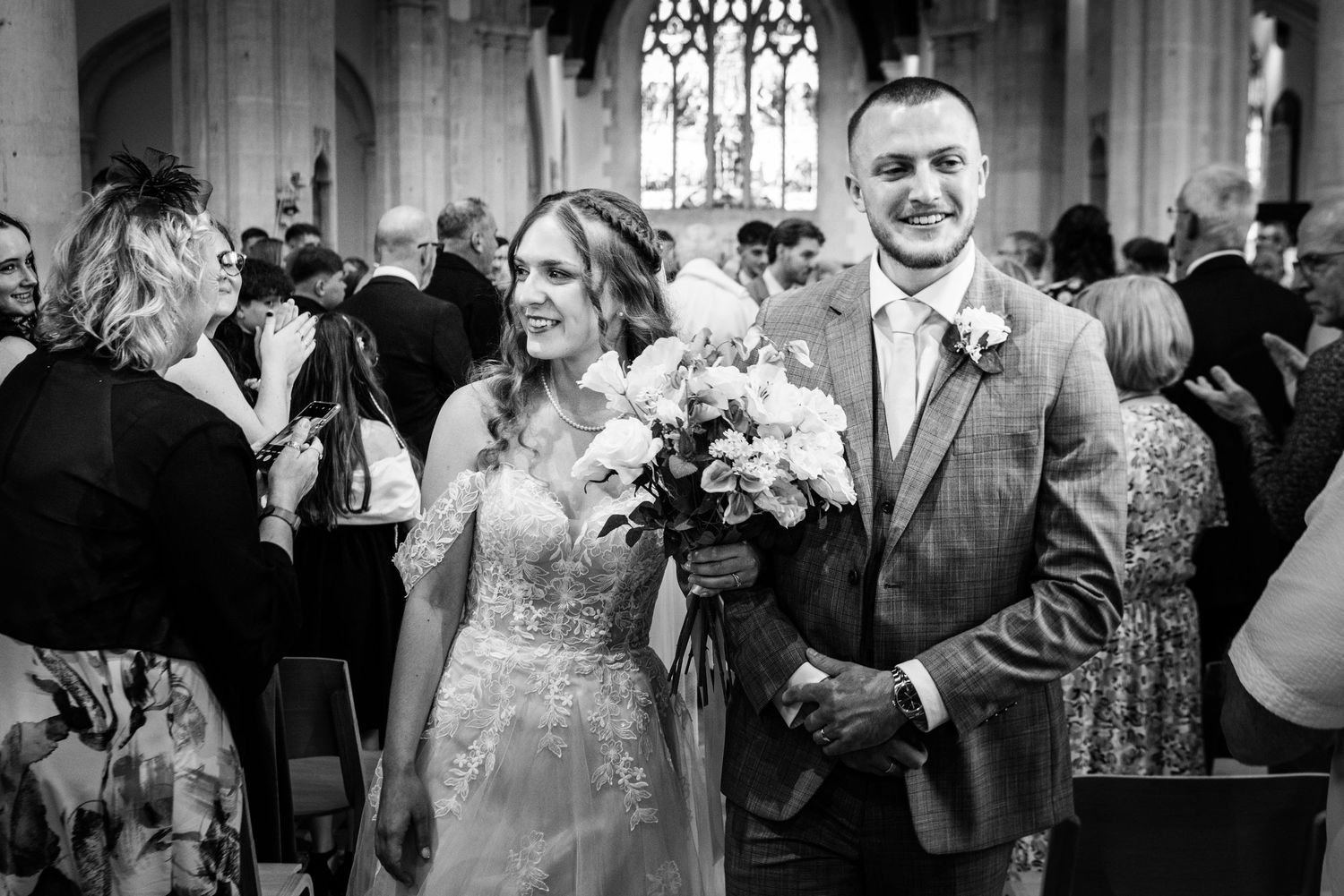 Newlyweds walking down the aisle in a church surrounded by smiling wedding guests.
