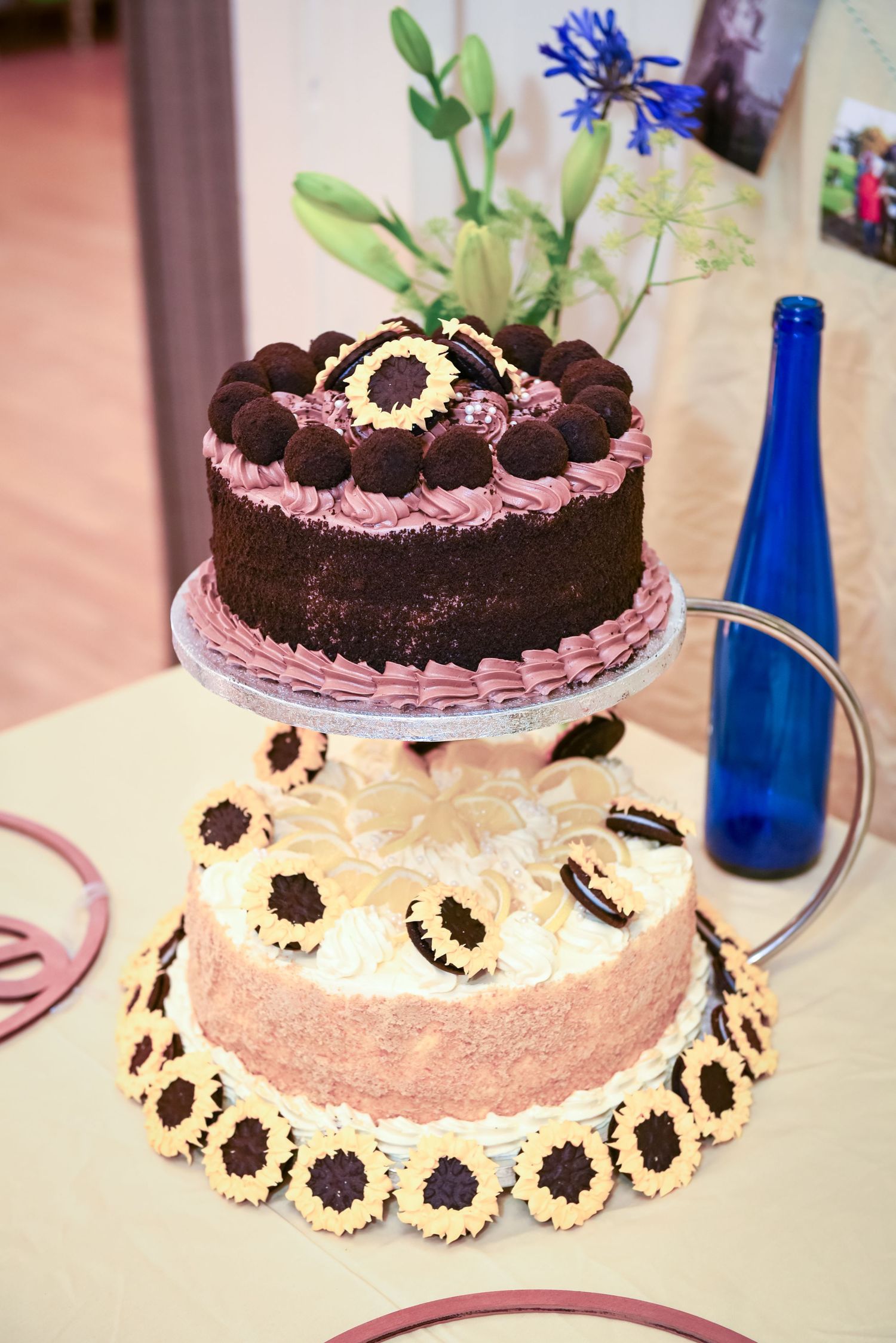 Two-tier chocolate and cream cake with Oreo cookies and sunflower decorations on a table with a blue bottle.