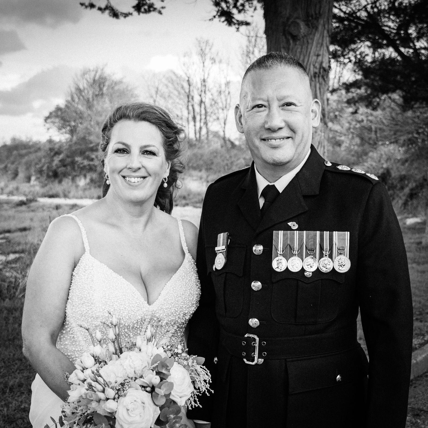 Black and white wedding photo of a smiling bride holding bouquet beside a man in military uniform with medals.