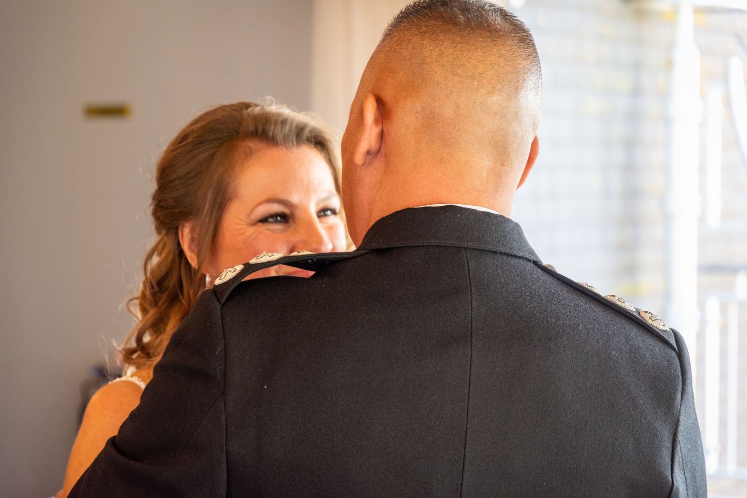 A bride smiles warmly at her groom in military dress uniform during an intimate wedding moment.