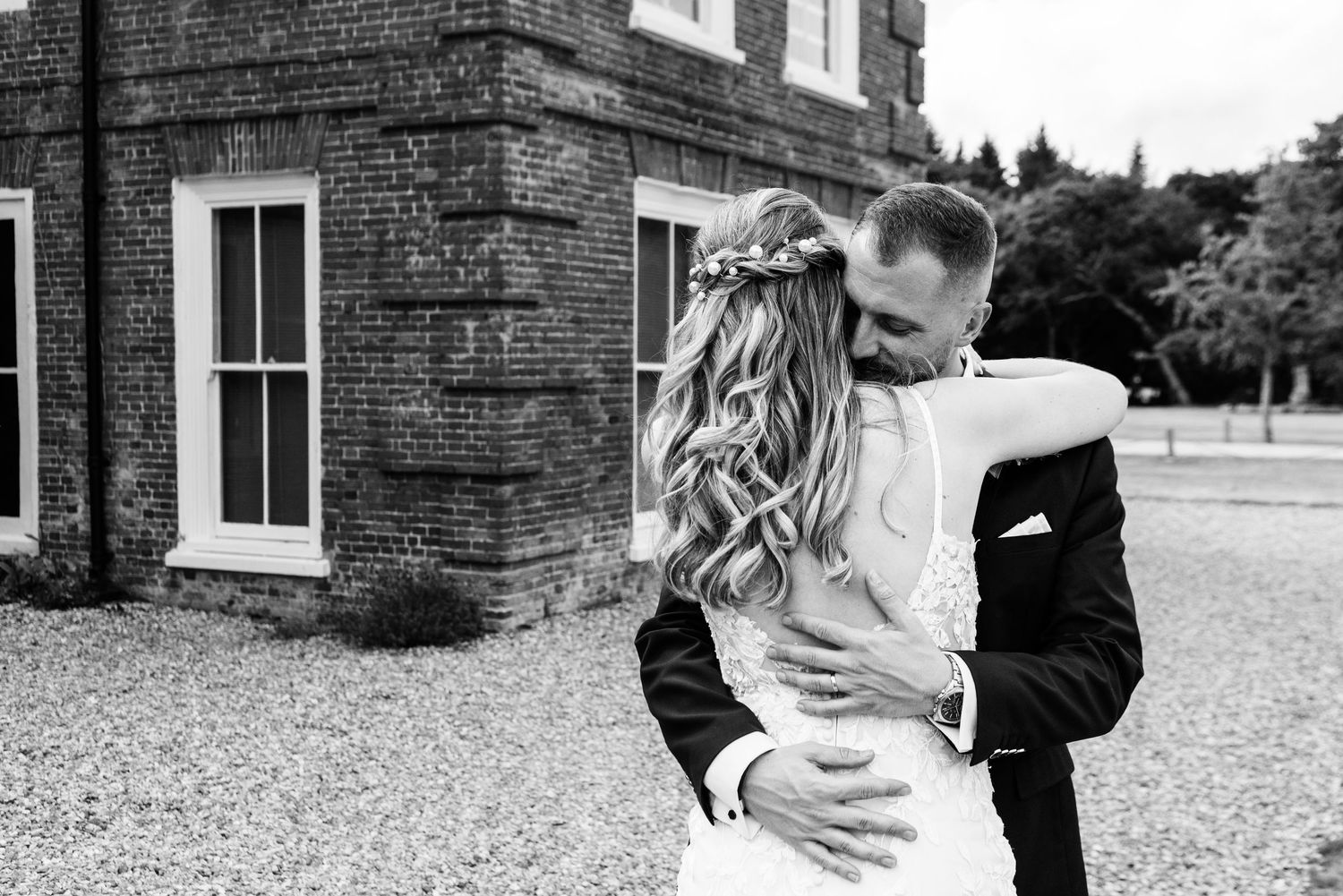 Black and white photo of a bride and groom embracing outside a brick building on their wedding day.