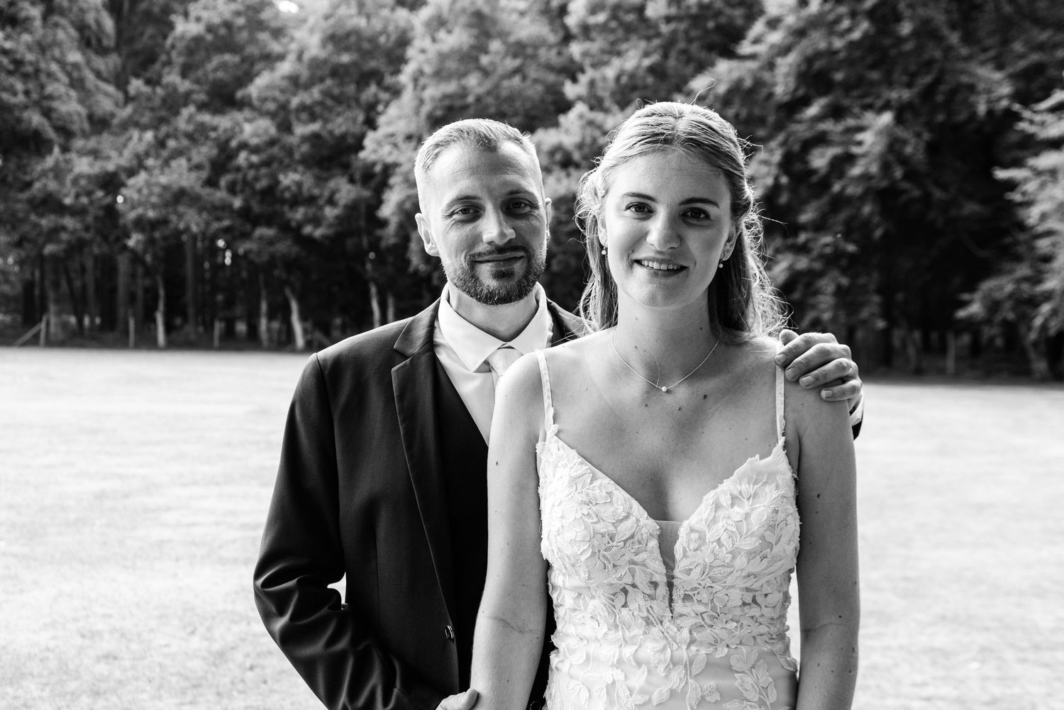 Black and white photo of a smiling bride and groom posing outdoors on their wedding day.