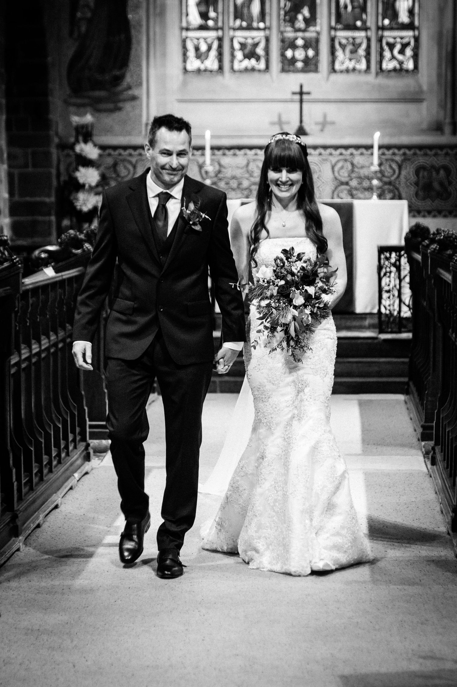 Black and white photo of a smiling bride and groom walking down the church aisle after their wedding ceremony.