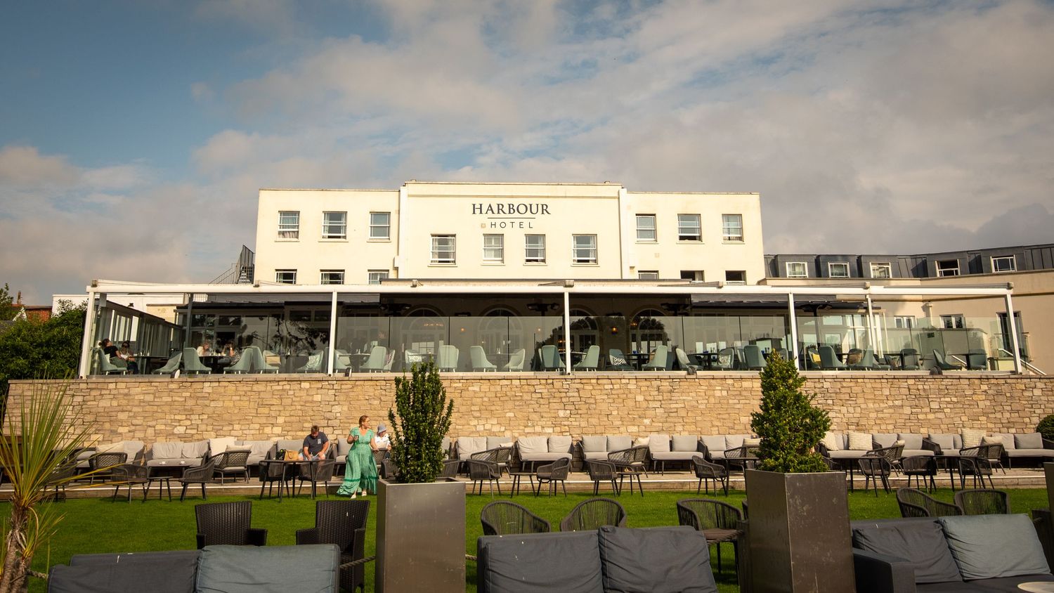 Modern white hotel building with stone terraces and landscaping under cloudy skies.