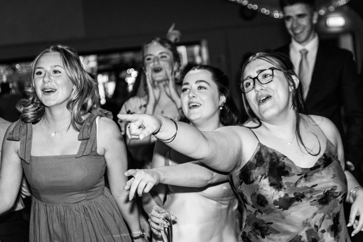 Wedding guests dancing and singing joyfully on the dance floor at a lively reception.