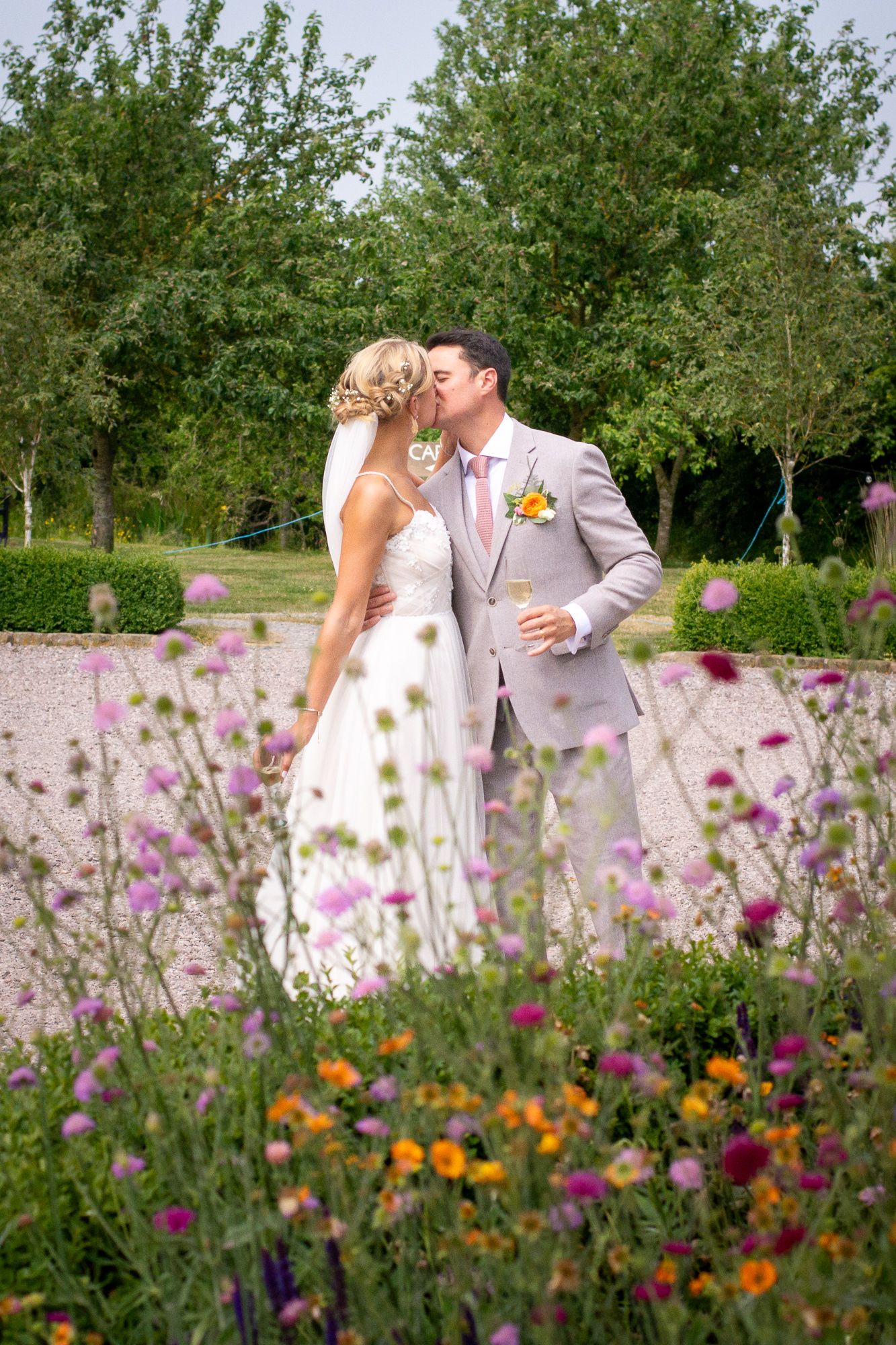Bride and groom sharing a kiss surrounded by colorful wildflowers in a lush garden setting.