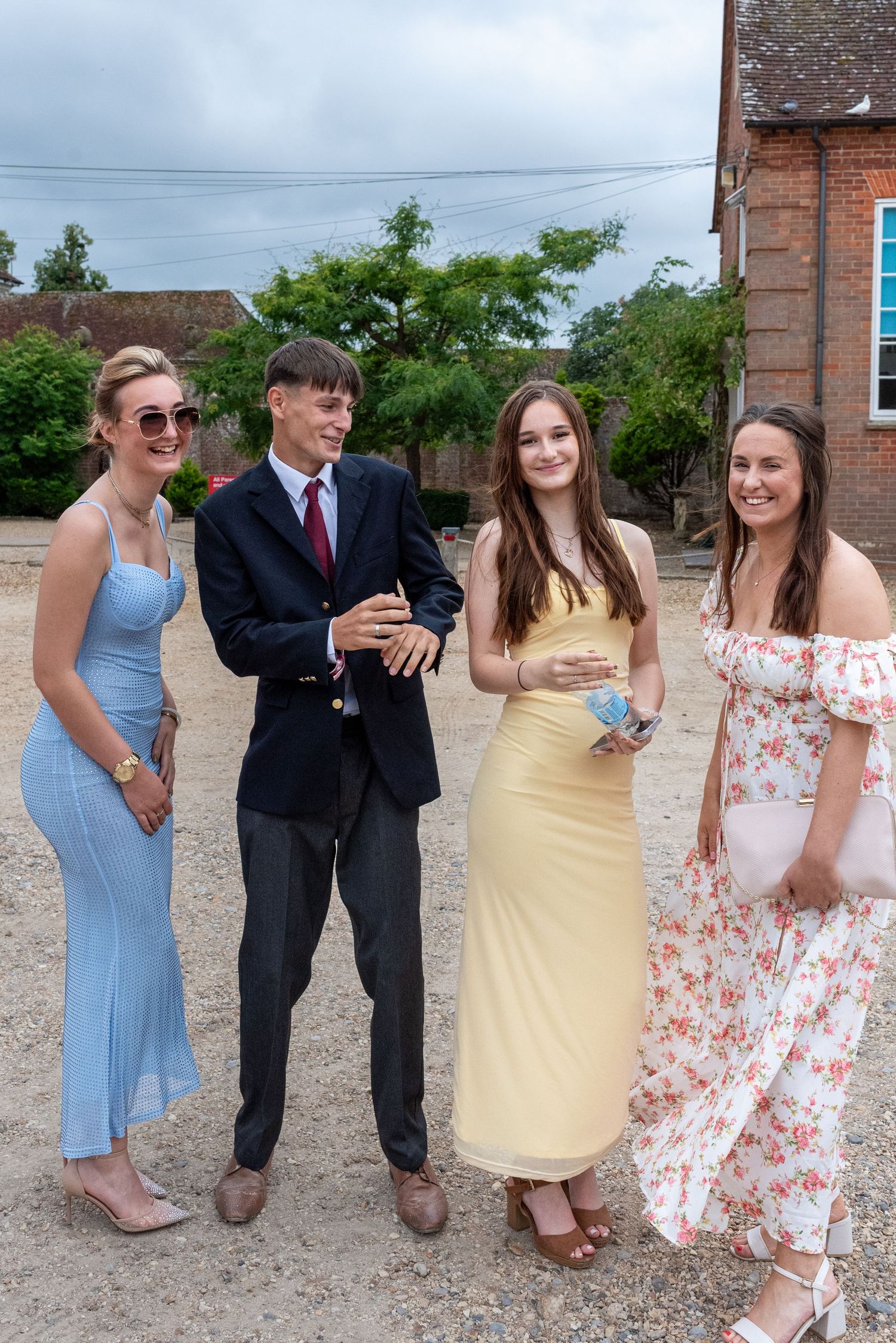 Four young people dressed in formal attire smile together outdoors at a summer event.