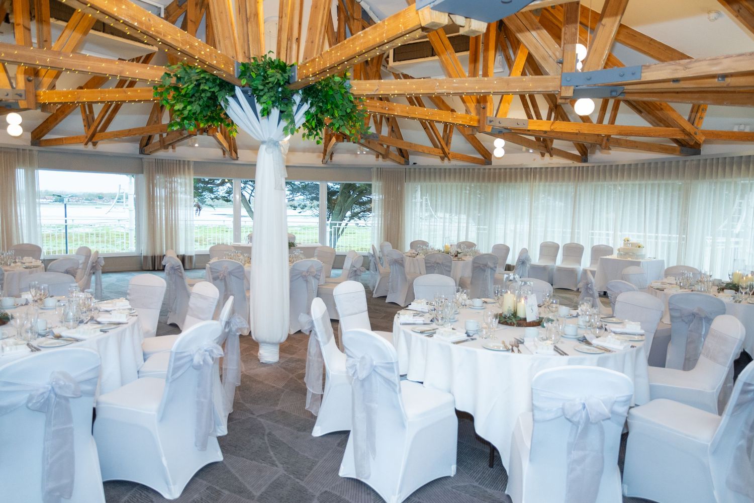 An elegant wedding reception venue with white chair covers, round tables, and tall floral centerpieces.