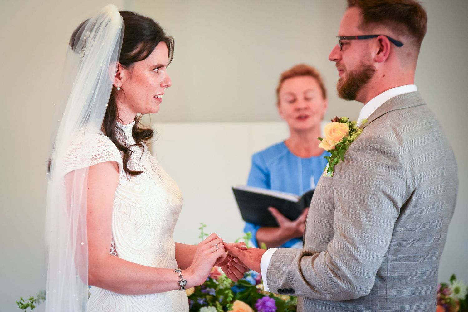 Bride and groom exchanging rings during wedding ceremony with officiant in background.