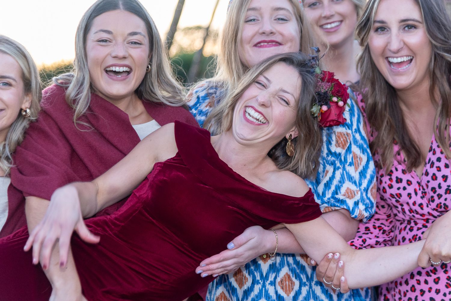 Group of joyful women laughing together outdoors, wearing colorful dresses in red, blue, and pink.