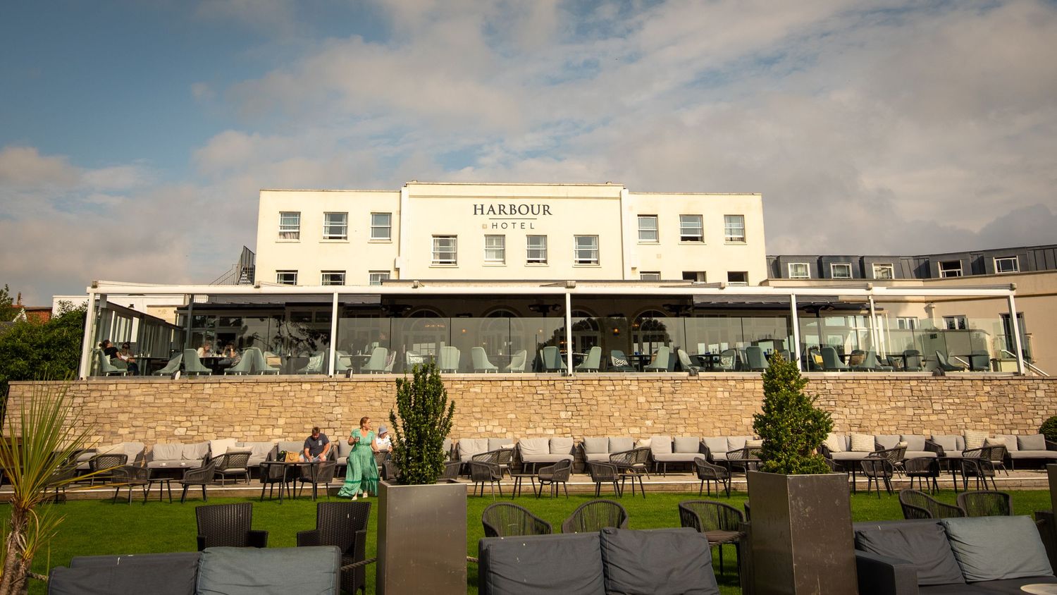 A modern white hotel building with glass windows and outdoor seating area under cloudy skies.