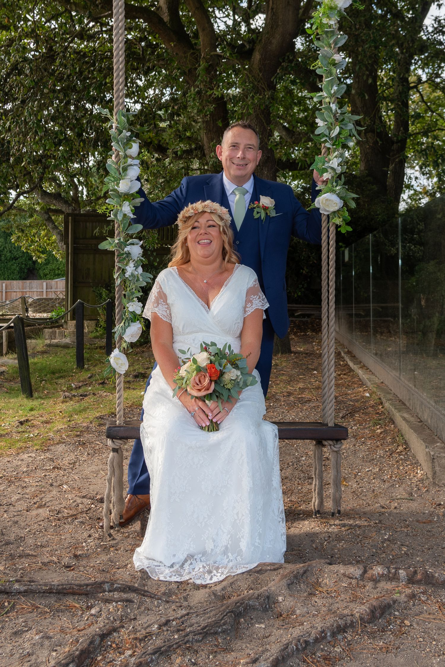 Bride sits on a rustic swing as groom stands behind her holding the ropes.