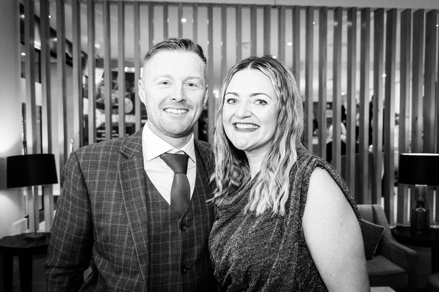 Smiling couple poses together in black and white photo at elegant indoor venue event.