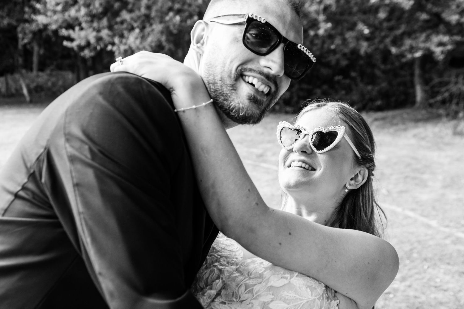 Black and white photo of a joyful couple in sunglasses embracing and laughing outdoors.
