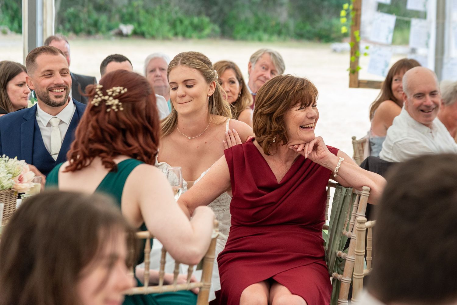 Bride comforts emotional woman in red dress during wedding ceremony while guests look on.