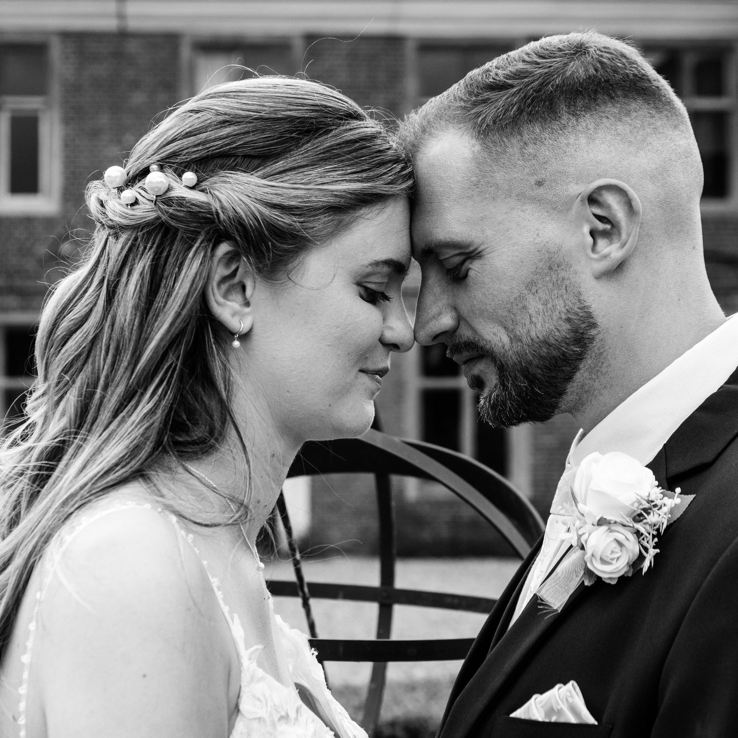 Romantic black and white portrait of bride and groom touching foreheads outside wedding venue.