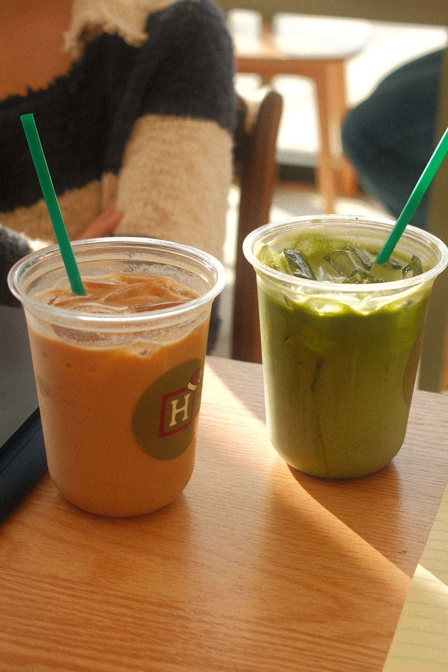 Two iced drinks on a wooden table, one a latte and one a green matcha with green straws.